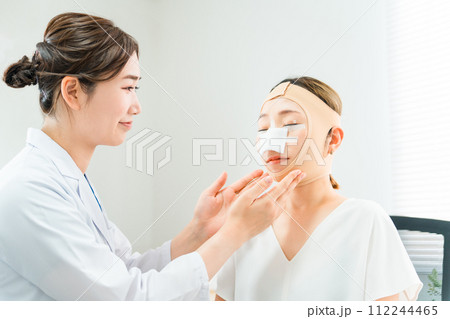 美容外科で整形手術を受けて術後に医師から診察を受ける女性 112244465