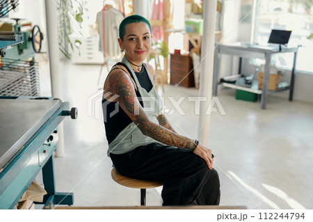 Creative female designer sitting on background of print machine in workshop 112244794