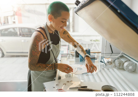 Smiling female worker preparing screen printing film while using printing machine in a workshop 112244808