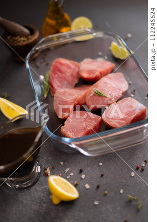 Pieces of Fresh tuna Fish fillet in glass cooking dish and soy sauce marinade in a gravy boat Pieces of Fresh tuna Fish fillet in glass cooking dish and soy sauce marinade in a gravy boat 112245624