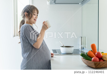 朝、家のキッチンで水・ぬるま湯・白湯を飲む妊婦の女性・マタニティ・プレママ 112246401