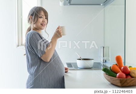 朝、家のキッチンで水・ぬるま湯・白湯を飲む妊婦の女性・マタニティ・プレママ 朝、家のキッチンで水・ぬるま湯・白湯を飲む妊婦の女性・マタニティ・プレママ 112246403