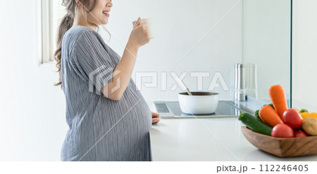 朝、家のキッチンで水・ぬるま湯・白湯を飲む妊婦の女性・マタニティ・プレママ 朝、家のキッチンで水・ぬるま湯・白湯を飲む妊婦の女性・マタニティ・プレママ 112246405