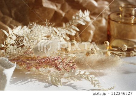 茶色の蝋引き紙の上に置かれた白を基調としたドライフラワーと茶色の小さな花瓶 茶色の蝋引き紙の上に置かれた白を基調としたドライフラワーと茶色の小さな花瓶 112246527