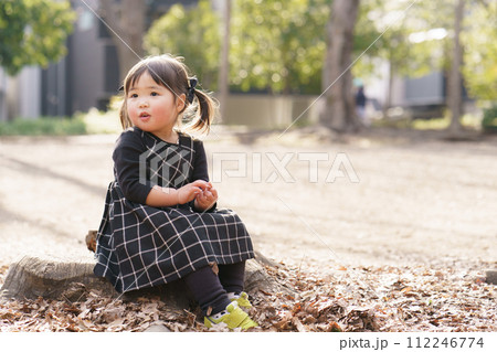 公園の切り株に座る小さな女の子 公園の切り株に座る小さな女の子 112246774