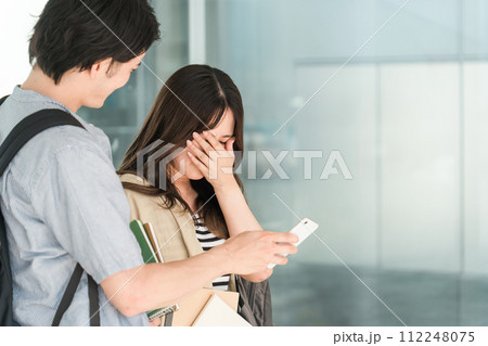 スマホを見ながら会話する学生・大学生の男女（泣く・困る・悲しい・落ち込む・悔しい）） 112248075