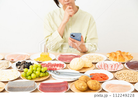 色々な食材とスマホを見ながら悩むミドル女性 112249228