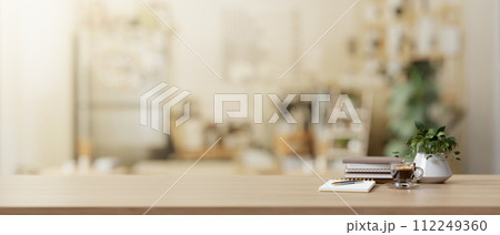 A copy space on a wooden desk features books, a coffee cup, and a potted plant in a living room. A copy space on a wooden desk features books, a coffee cup, and a potted plant in a living room. 112249360