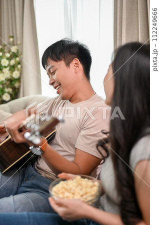 Happy Asian couple enjoying playing guitar and singing at home, having a cute romantic time together Happy Asian couple enjoying playing guitar and singing at home, having a cute romantic time together 112249666