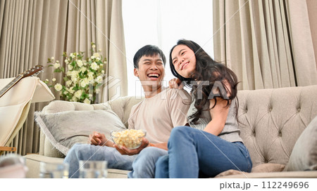 A cheerful Asian couple is watching an exciting sports match or game show together at home. 112249696