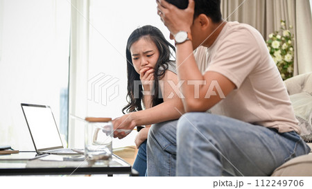 An unhappy young Asian couple is arguing about high domestic bills on a sofa in the living room. 112249706