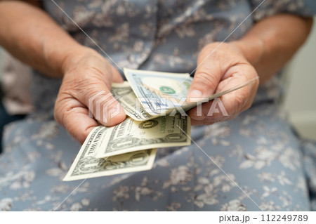 Asian senior woman holding and counting US dollar banknotes money in purse. Poverty, saving problem in retirement. 112249789