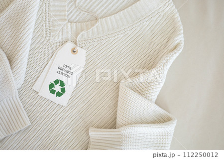 White knitted clothing with a white label that says 100% organic cotton and features a recycling symbol. White knitted clothing with a white label that says 100% organic cotton and features a recycling symbol. 112250012