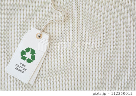 White knitted clothing with a white label that says 100% recyclable fabric and features a recycling symbol. 112250013