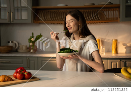 Young Woman Enjoying a Fresh Green Salad in Her Sunny Kitchen During Breakfast Young Woman Enjoying a Fresh Green Salad in Her Sunny Kitchen During Breakfast 112251825