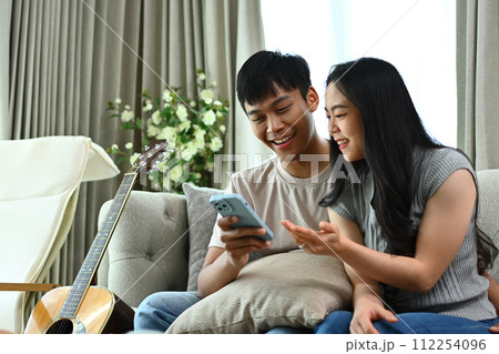 Happy young couple using mobile phone for shopping on Internet while sitting on couch Happy young couple using mobile phone for shopping on Internet while sitting on couch 112254096