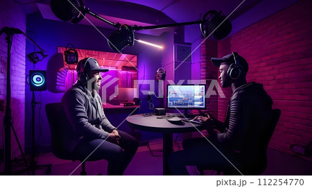 Two men wearing headphones are sitting in a room with purple lig 112254770
