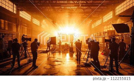 AI-generated content. Warm light on film set bathed, creating silhouette effect. Indoor space with natural light. Crew members working with filming equipment. 112255815