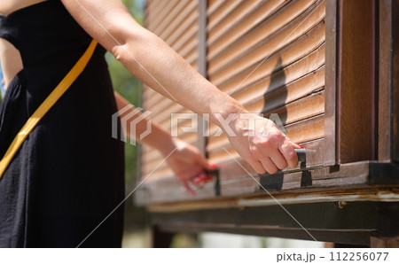 Female hands hold wooden latch handles open wooden blinds outdoors closeup Female hands hold wooden latch handles open wooden blinds outdoors closeup 112256077