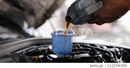 Mechanic pouring engine oil into engine in car service 112256200