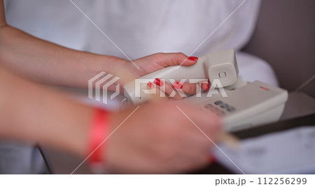 Woman dials phone number in the hotel rooms to communicate with reception 112256299