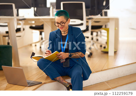 Creative smiling tattooed business woman with green short hair working on laptop in modern office 112259179
