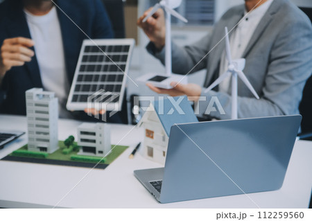 Two Young Engineers Expertise in Solar Cell Installation Meetings and Discussion in The Job. Planning to Install Solar Photovoltaic Panels on Roof Top in The Office Room with Factory Building Plan. 112259560
