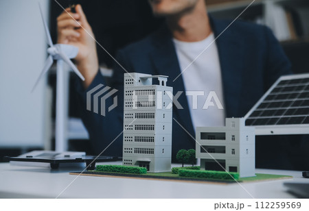 Two Young Engineers Expertise in Solar Cell Installation Meetings and Discussion in The Job. Planning to Install Solar Photovoltaic Panels on Roof Top in The Office Room with Factory Building Plan. 112259569