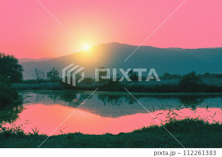 Mountain landscape in the evening. Beautiful lake against mountains. The Hula Valley in northern Israel at sunset Mountain landscape in the evening. Beautiful lake against mountains. The Hula Valley in northern Israel at sunset 112261383