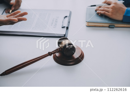 Justice and Law concept. Legal counsel presents to the client a signed contract with gavel and legal law or legal having team meeting at law firm in background 112262616