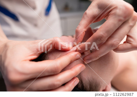 Close-up shot of a woman's head doing a facial massage on a treatment table. Therapist applying pressure with thumbs on forehead 112262987