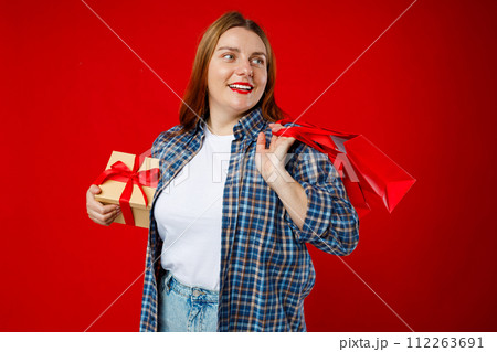Portrait of cheerful, happy woman smiling excited. Girl holding wrapped present and paper bags, celebrating birthday or sales on red background. Valentine's Day Women's Day birthday holiday concept. Portrait of cheerful, happy woman smiling excited. Girl holding wrapped present and paper bags, celebrating birthday or sales on red background. Valentine's Day Women's Day birthday holiday concept. 112263691