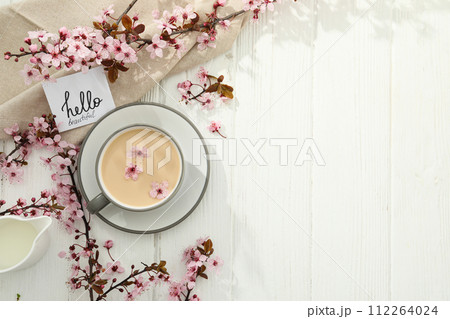 Spring twigs with flowers with a cup of hot drink, on a light wooden background. 112264024