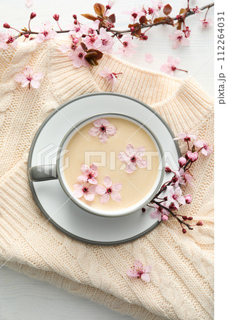Spring twigs with flowers with a cup of hot drink, on a light wooden background. 112264031