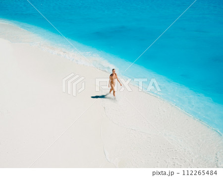 Woman in swimsuit walking on tropical white sandy beach with turquoise ocean water. Aerial view Woman in swimsuit walking on tropical white sandy beach with turquoise ocean water. Aerial view 112265484