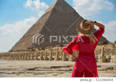 A girl in a red dress looks at an Egyptian pyramid A girl in a red dress looks at an Egyptian pyramid 112266064