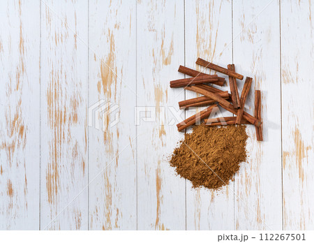 cinnamon sticks and cinnamon powder on a white wooden table, top view. cinnamon sticks and cinnamon powder on a white wooden table, top view. 112267501