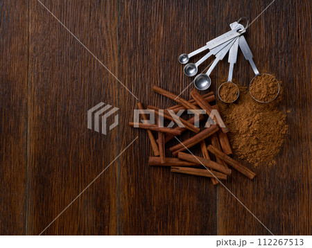 cinnamon powder poured out of a measuring spoon on a dark wooden table , top view. cinnamon powder poured out of a measuring spoon on a dark wooden table , top view. 112267513