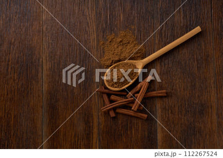 cinnamon powder in a wooden spoon on a dark wooden table , top view. 112267524