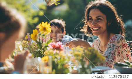 AI-generated content. A joyful woman enjoys sunny garden party and reaches for food at a table decorated with flowers. Holiday dinner in backyard, family traditions 112270127