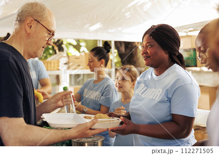 Multiethnic volunteering crew, serving fresh food to those in need, offering support and relief to homeless people and refugees. Poor and hungry individuals receiving free meals at outdoor food bank. Multiethnic volunteering crew, serving fresh food to those in need, offering support and relief to homeless people and refugees. Poor and hungry individuals receiving free meals at outdoor food bank. 112271505
