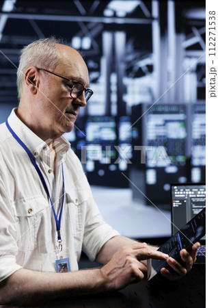 Senescent IT developer coding in high tech data center using javascript language. Qualified professional updating software on server rigs on laptop terminal, ensuring optimal performance and security 112271538