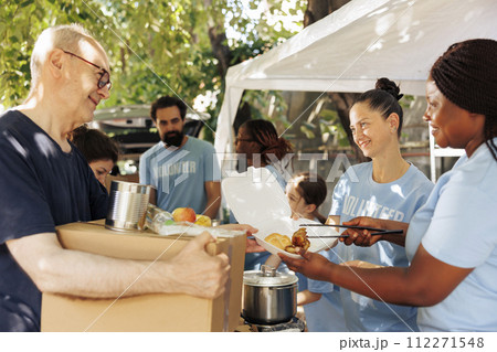 Charity wokers happily provide food donations to the poor, including homeless individuals and seniors. Hunger relief team distribute meal boxes and packages of canned goods with genuine smiles. 112271548