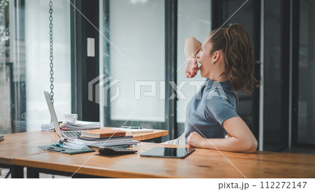 A woman experiences a moment of fatigue, yawning as she works on her laptop, signaling a need for a brief respite in her focused workday. A woman experiences a moment of fatigue, yawning as she works on her laptop, signaling a need for a brief respite in her focused workday. 112272147