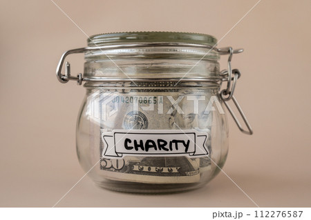 Saving Money In Glass Jar filled with Dollars banknotes. CHARITY transcription in front of jar. Managing personal finances extra income for future insecurity Saving Money In Glass Jar filled with Dollars banknotes. CHARITY transcription in front of jar. Managing personal finances extra income for future insecurity 112276587