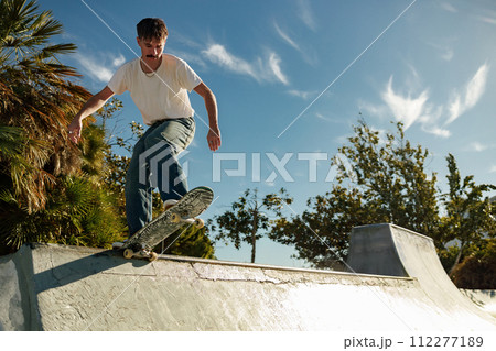 Active young man riding skateboard in skate park on sunny day. Extreme sport concept Active young man riding skateboard in skate park on sunny day. Extreme sport concept 112277189