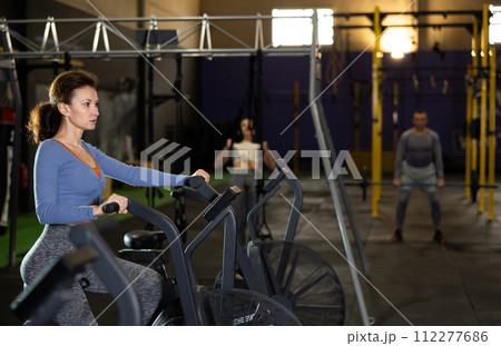 Concentrated woman working out on stationary air bicycle in gym Concentrated woman working out on stationary air bicycle in gym 112277686