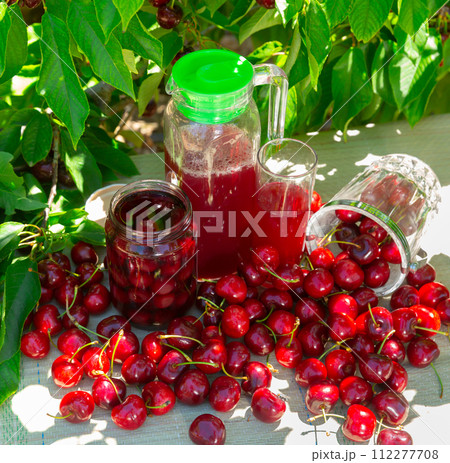 Fresh sweet cherries, mason jar of compote and juice in carafe in orchard 112277708