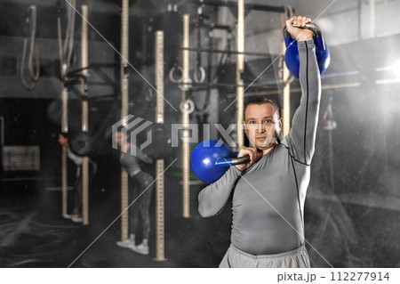 Man performing kettlebell overhead press during strength training 112277914