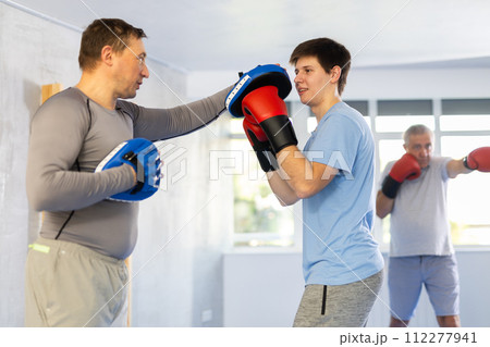 Guy in boxing gloves punching mitts in hands of instructor at self-defense class 112277941
